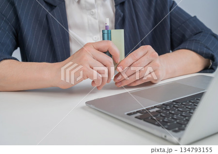 Business woman smoking an electronic cigarette while working on a laptop. Tobacco heating system.  134793155