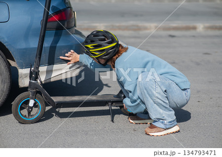 A distressed woman examines the damage after a collision between an electric scooter and a car. 134793471