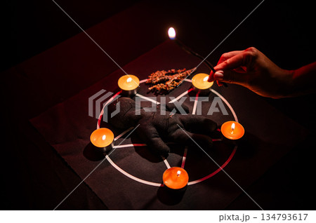 Woman drips wax from black candle onto voodoo doll. Woman drips wax from black candle onto voodoo doll. 134793617