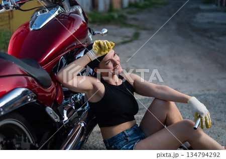 Brunette woman in denim shorts repairs a red motorcycle.  134794292