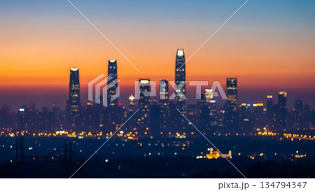Blurred city skyline at sunset showing bokeh lights of buildings. Abstract urban landscape for background or design element. Modern metropolis view. Blurred city skyline at sunset showing bokeh lights of buildings. Abstract urban landscape for background or design element. Modern metropolis view. 134794347