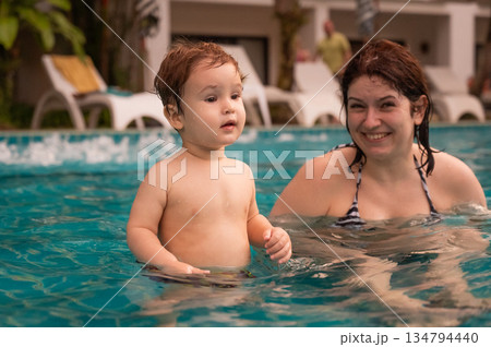 Caucasian woman holds her son while swimming in a pool on vacation. Mom teaches little boy to swim. Caucasian woman holds her son while swimming in a pool on vacation. Mom teaches little boy to swim. 134794440