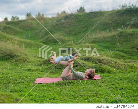 Caucasian woman doing yoga with her little son outdoors. Caucasian woman doing yoga with her little son outdoors. 134794574