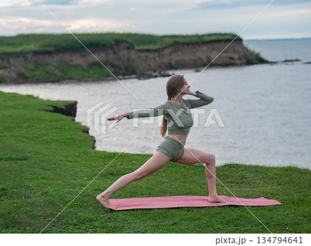 Caucasian woman doing yoga on the river bank. Warrior pose. Caucasian woman doing yoga on the river bank. Warrior pose. 134794641