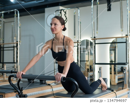 Caucasian woman doing exercises on reformer machine. Caucasian woman doing exercises on reformer machine. 134794697