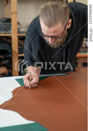 Caucasian bearded man working as a tanner in a workshop. Caucasian bearded man working as a tanner in a workshop. 134794886