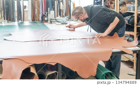 Caucasian bearded man working as a tanner in a workshop. Caucasian bearded man working as a tanner in a workshop. 134794889