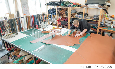 Caucasian bearded man working as a tanner in a workshop. Caucasian bearded man working as a tanner in a workshop. 134794900
