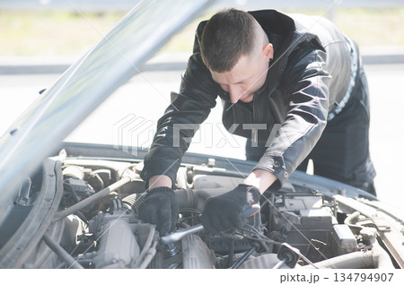 A man changes spark plugs in his car. A man changes spark plugs in his car. 134794907