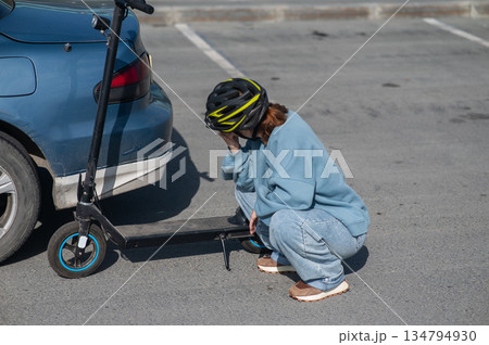 A distressed woman examines the damage after a collision between an electric scooter and a car. A distressed woman examines the damage after a collision between an electric scooter and a car. 134794930