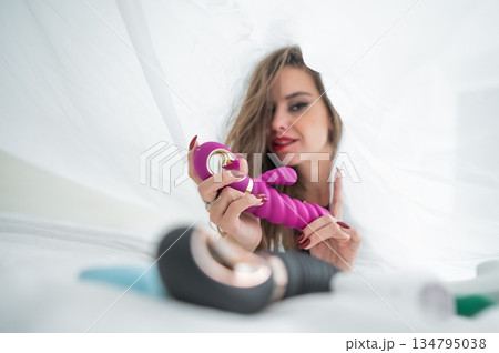 Woman in lace lingerie holds a dildo. A beautiful Caucasian woman lies under the sheets and holds a dildo.  134795038