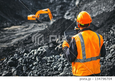 Construction Worker in Orange Safety Vest and Helmet Operating Device on Job Site Construction Worker in Orange Safety Vest and Helmet Operating Device on Job Site 134796704
