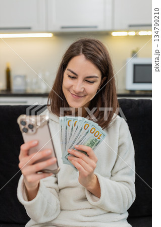 Woman counts money dollar cash checks rate on smartphone smiles plans dream buy salary savings bonus Woman counts money dollar cash checks rate on smartphone smiles plans dream buy salary savings bonus 134799210