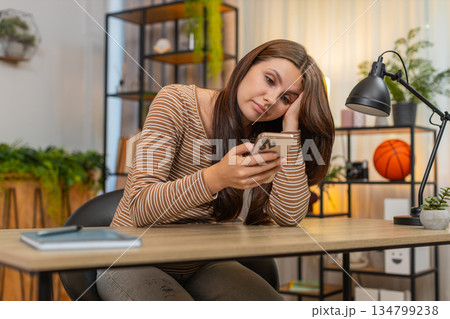 Young woman scrolls smartphone news feed bored unhappy drained by dull repetitive social media posts 134799238