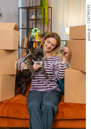 Middle-aged woman with dog jingles keys for new flat makes victory sign boxes stacked after move joy Middle-aged woman with dog jingles keys for new flat makes victory sign boxes stacked after move joy 134799241