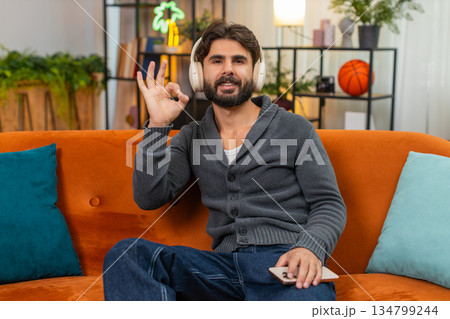 Indian man wears wireless headphones listens nature sound meditates calm smiles gives approval sign 134799244
