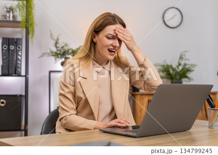 Businesswoman faces laptop system crash data loss holds head facepalm error pops up failure reaction Businesswoman faces laptop system crash data loss holds head facepalm error pops up failure reaction 134799245