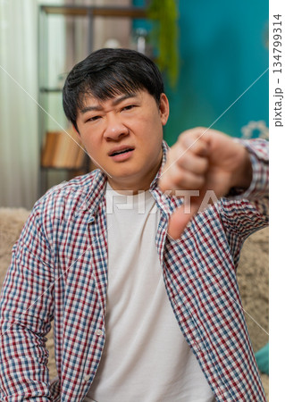 Asian man showing thumbs down, unhappy dislike expression signaling strong negative disagreement Asian man showing thumbs down, unhappy dislike expression signaling strong negative disagreement 134799314