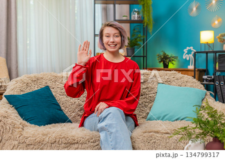 Young woman happily waving hand hello gesture friendly cheerful greeting expression smiling joyfully 134799317