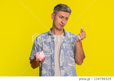 Man holding piggy bank dropping last coin sighing showing saving effort or poor money condition 134799329