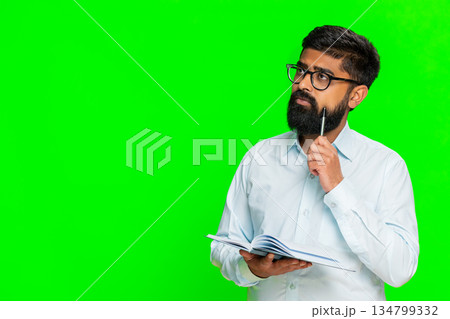 Indian man writing in notebook focused face planning daily tasks to-do list concentration gesture 134799332