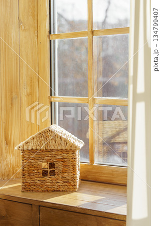 Small woven house model on sunny wooden window sill against natural light window in child room 134799407