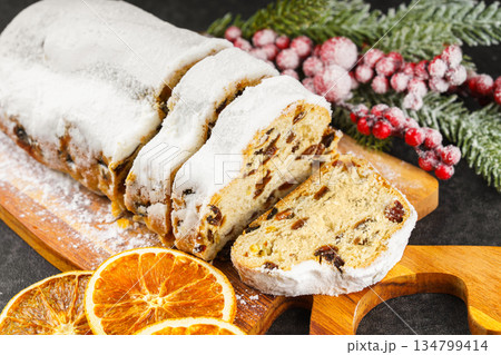 Traditional sliced Christmas stollen loaf with raisins and powdered sugar on wooden cutting board 134799414