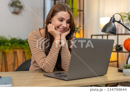 Young woman looks at laptop screen watches online travel advert leans on hands dreams about vacation 134799644