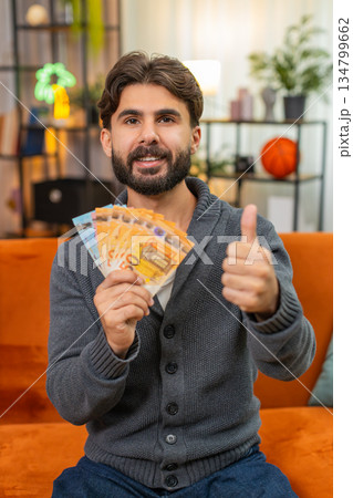 Indian man counts euro cash banknotes dreams of travel thinks where to spend money smiles very happy 134799662