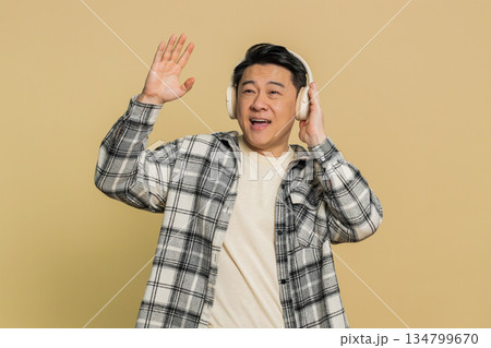 Happy Asian man listening music on headphones and dancing disco fooling around having fun Happy Asian man listening music on headphones and dancing disco fooling around having fun 134799670