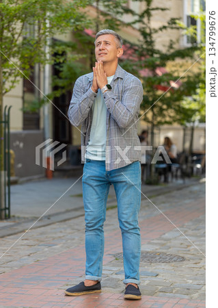 Caucasian mature man tourist praying with closed eyes to God asking for blessing on city town street Caucasian mature man tourist praying with closed eyes to God asking for blessing on city town street 134799676