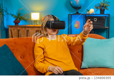 Teenager boy child excitedly playing VR, waving hands, showing WOW emotion, sitting on sofa at home Teenager boy child excitedly playing VR, waving hands, showing WOW emotion, sitting on sofa at home 134800305