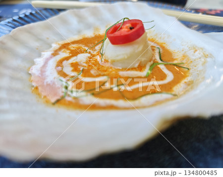 Appetizing gourmet scallop dish served directly inside beautiful white shell with rich orange curry sauce creamy coconut milk garnish red chili slice and herb for elegant seafood dining experience 134800485