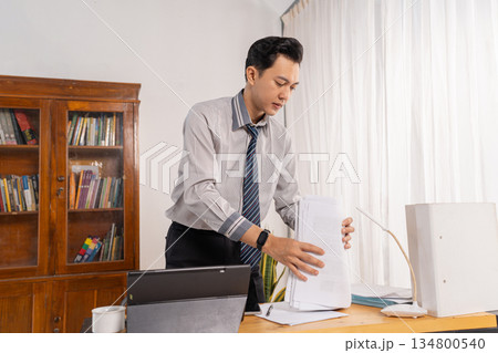 Office worker organizes documents amidst busy tasks at desk Office worker organizes documents amidst busy tasks at desk 134800540