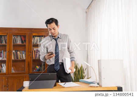 man juggling phone and paperwork during busy office call man juggling phone and paperwork during busy office call 134800541