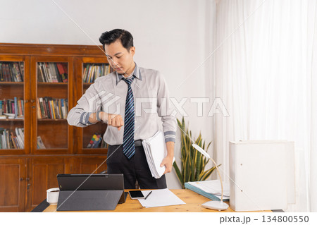 Male employee scrutinizing time as he handles paperwork at desk 134800550