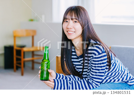 自宅のリビングでビールを飲む若い女性 自宅のリビングでビールを飲む若い女性 134801531