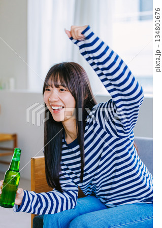 自宅でビールを飲んでスポーツ観戦する若い女性 自宅でビールを飲んでスポーツ観戦する若い女性 134801676