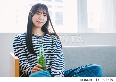 自宅のリビングでビールを飲む若い女性 134801719