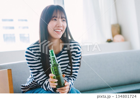自宅のリビングでビールを飲む若い女性 134801724