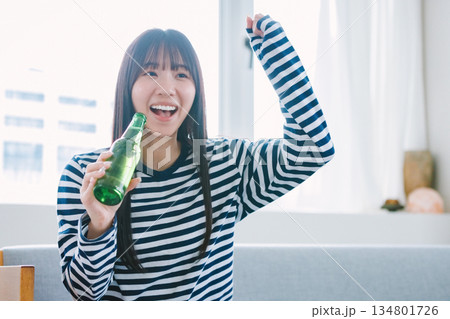 自宅でビールを飲んでスポーツ観戦する若い女性 134801726