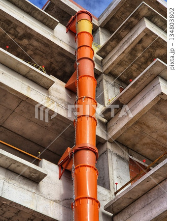 A bottom-up shot of an unfinished modern multi-story building with bare concrete floor slabs.  The bright orange construction waste pipe 134803802