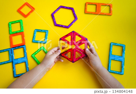 A child's creative play session with magnetic building blocks is captured against a bright yellow backdrop, showing various constructed shapes. A child's creative play session with magnetic building blocks is captured against a bright yellow backdrop, showing various constructed shapes. 134804148