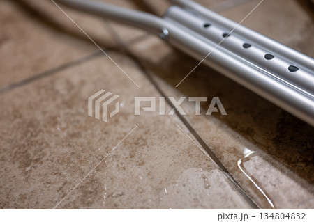 Water on the floor near metal crutches in a room with tile flooring in a bathroom 134804832