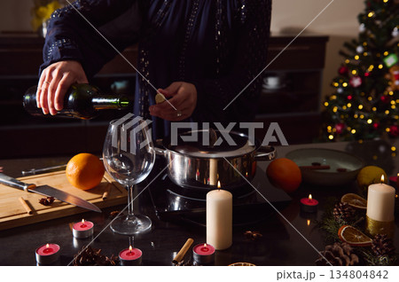 Winter Holiday Kitchen Scene With Woman Pouring Wine, Spices, Candles, And Christmas Tree Winter Holiday Kitchen Scene With Woman Pouring Wine, Spices, Candles, And Christmas Tree 134804842