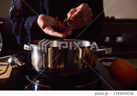 Winter Kitchen Scene: Woman Preparing Mulled Wine With Spices Beside A Pot And Orange 134804856