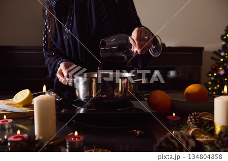 Elegant Woman In Evening Gown Preparing Mulled Wine For Winter Holidays By Candlelight Elegant Woman In Evening Gown Preparing Mulled Wine For Winter Holidays By Candlelight 134804858
