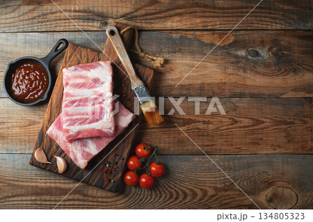Raw pork ribs with spices, salt and rosemary on dark wooden background Raw pork ribs with spices, salt and rosemary on dark wooden background 134805323