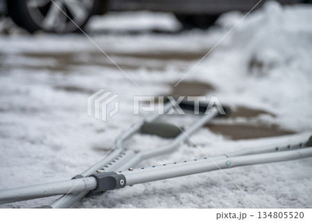 Crutches rest on snowy ground outside a car during winter weather in the late afternoon Crutches rest on snowy ground outside a car during winter weather in the late afternoon 134805520