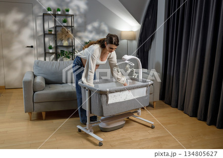 Pregnant woman arranging baby crib with mobile in nursery room preparing for newborn arrival Pregnant woman arranging baby crib with mobile in nursery room preparing for newborn arrival 134805627